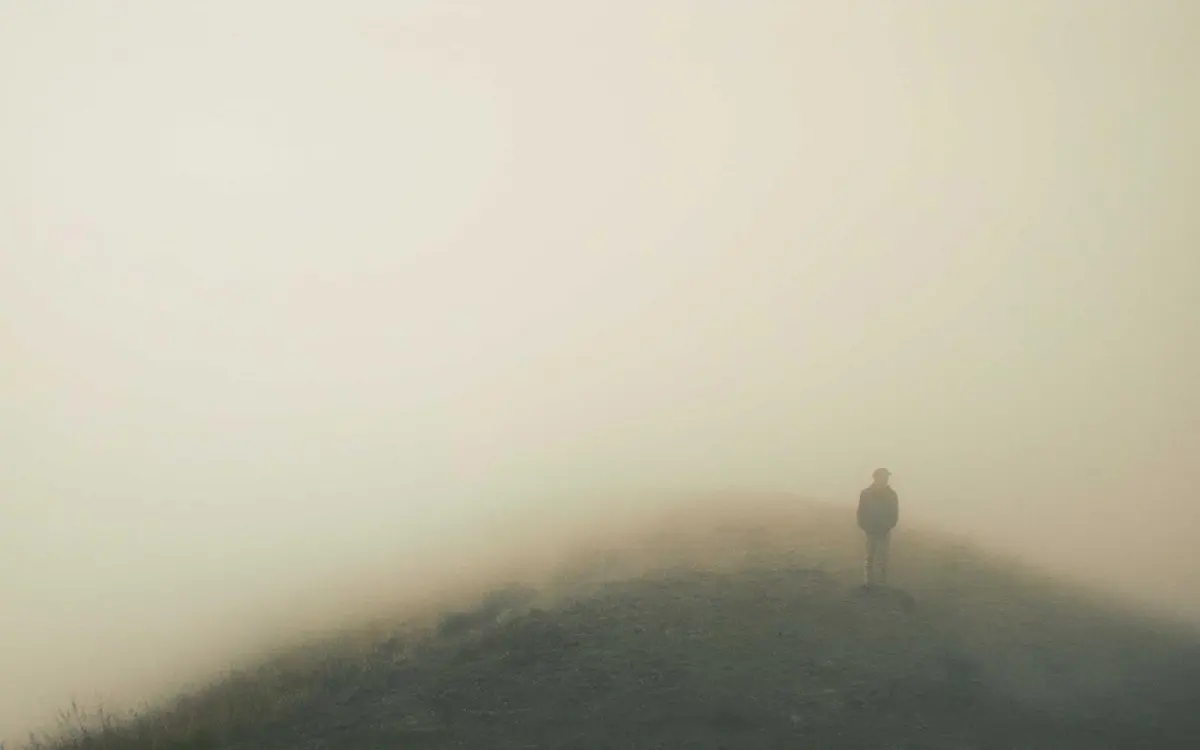 Una figura sola sobre una colina entre niebla beis